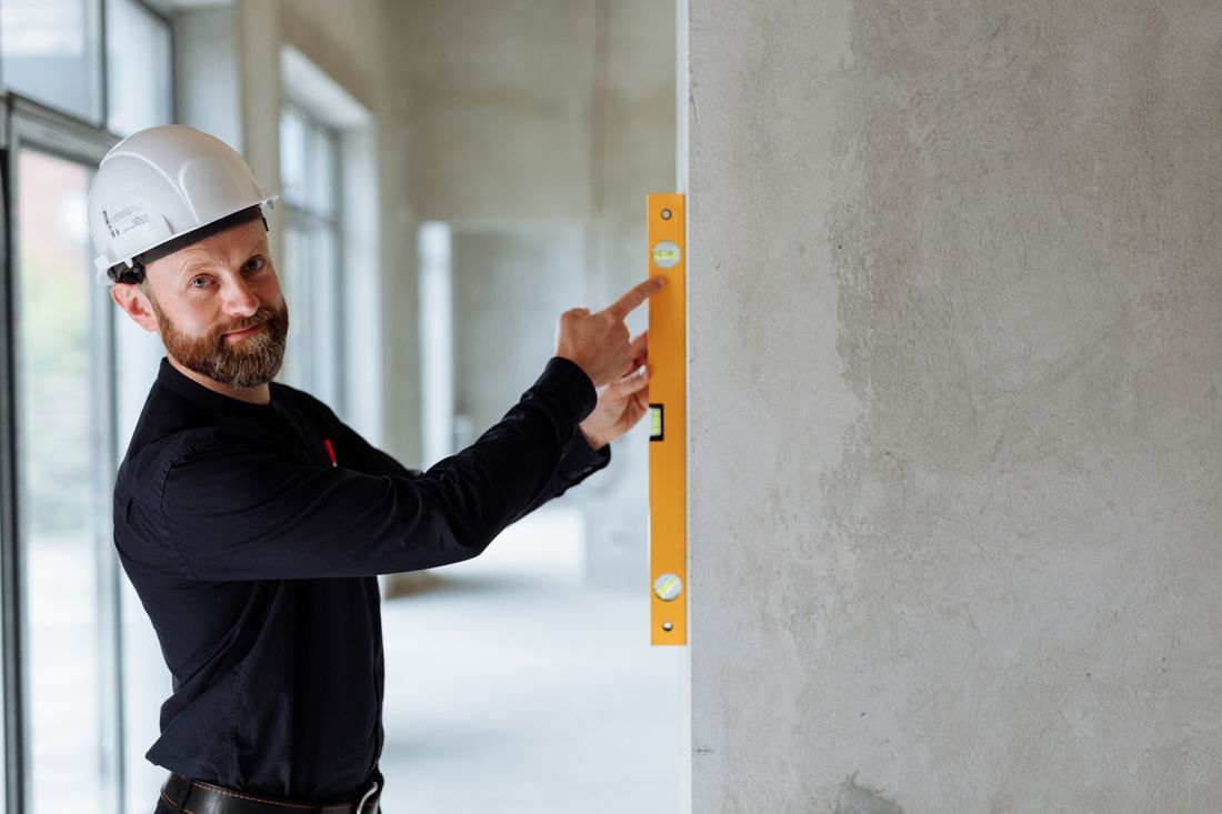 Bauarbeiter mit Schutzhelm prüft mit einer Wasserwaage eine Wand auf der Baustelle